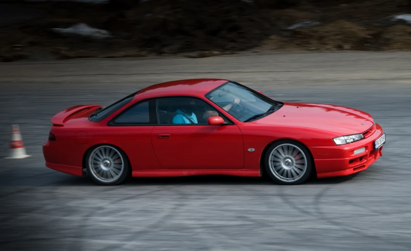 a red car with white trim driving on the street