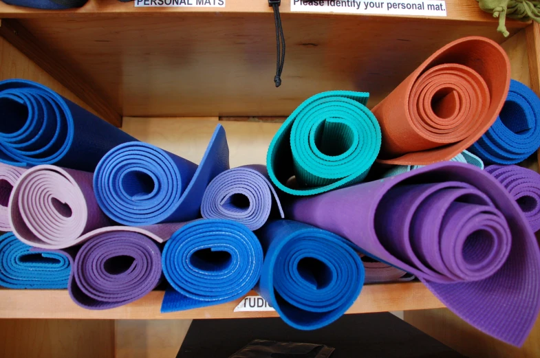 many colors of yoga mats are stacked up on a shelf