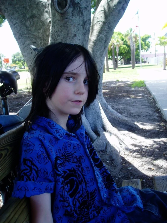 the girl is sitting on a bench near a tree