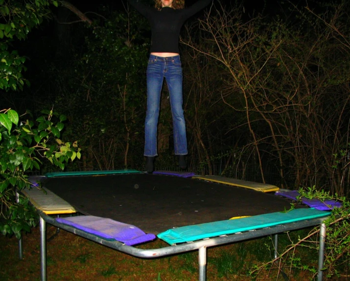 a woman posing on top of a trampoline in the middle of the woods