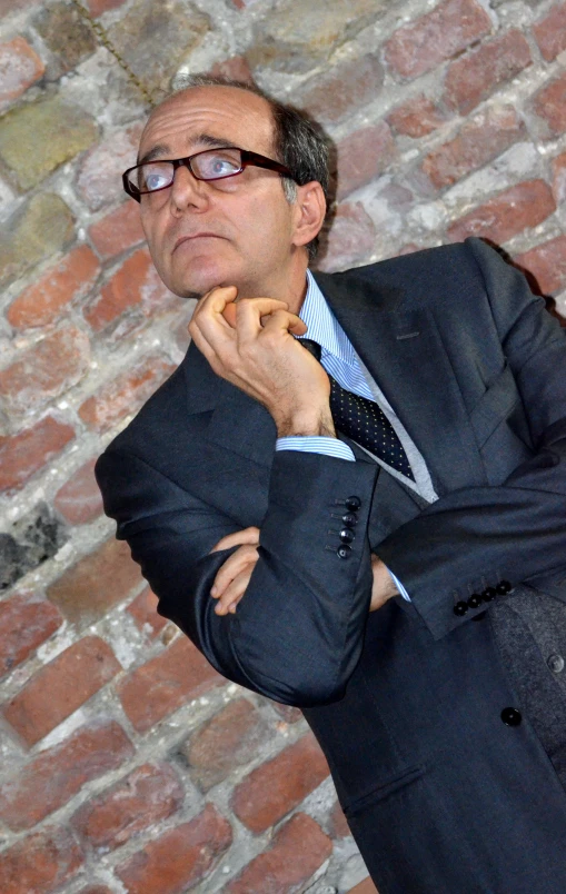 a man standing in front of a brick wall wearing a suit and tie