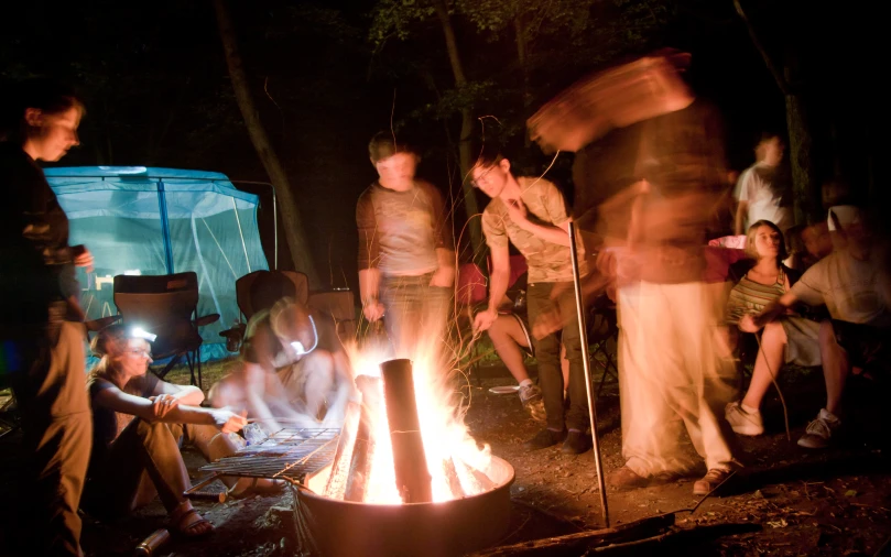 a group of people around a fire with a tent in the background