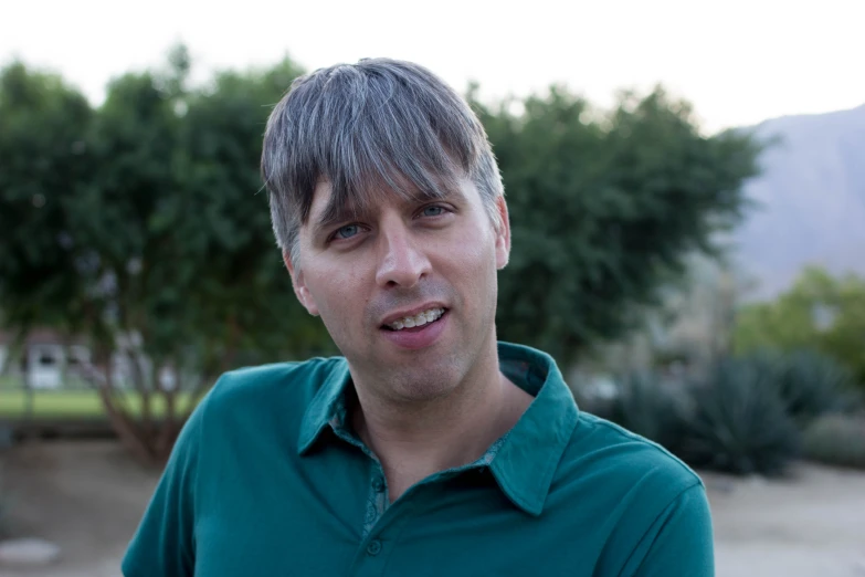 a man smiles for the camera in front of some bushes