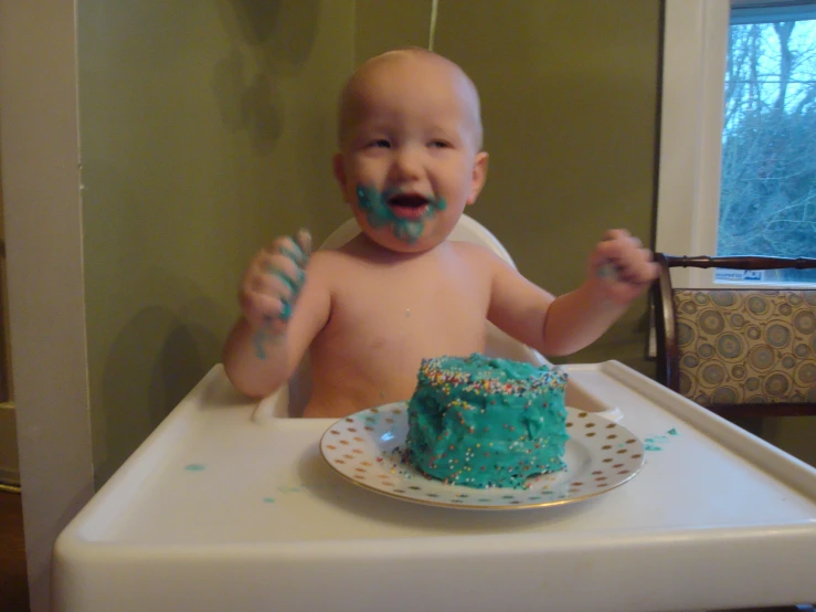a young baby with frosting on his face eating a green cake
