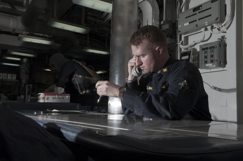 there is a male marine captain sitting on the boat talking on the phone