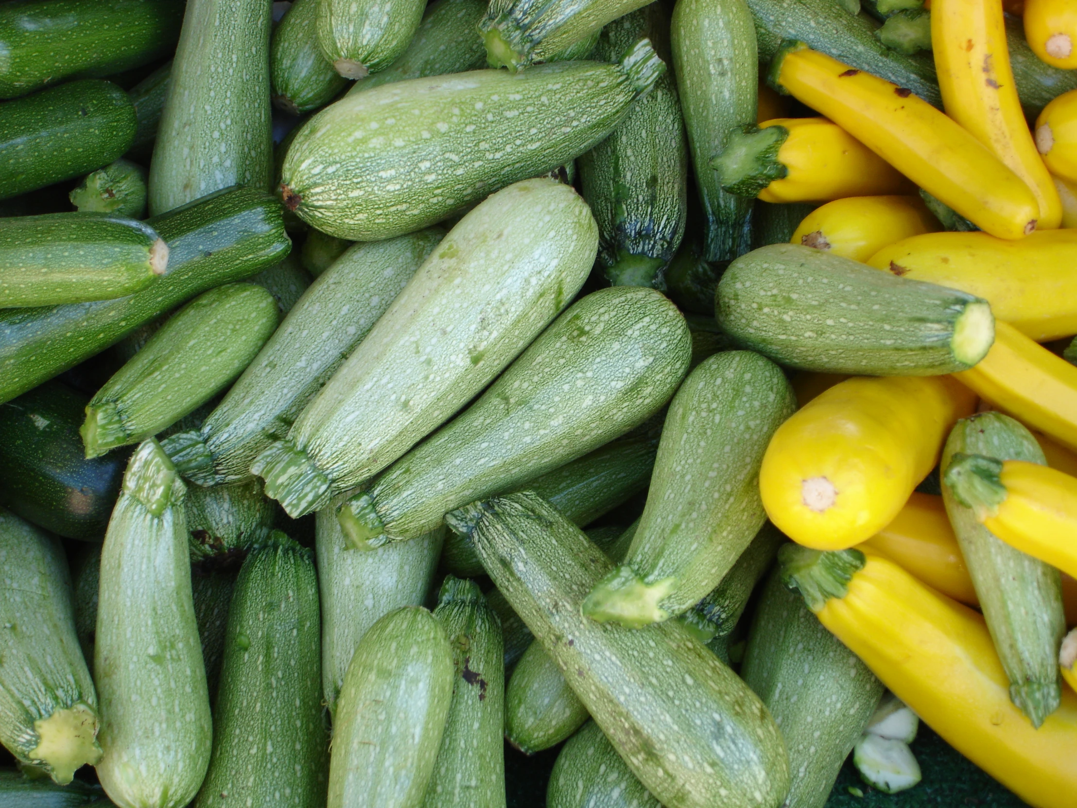 a pile of cucumbers in a basket with yellow ones