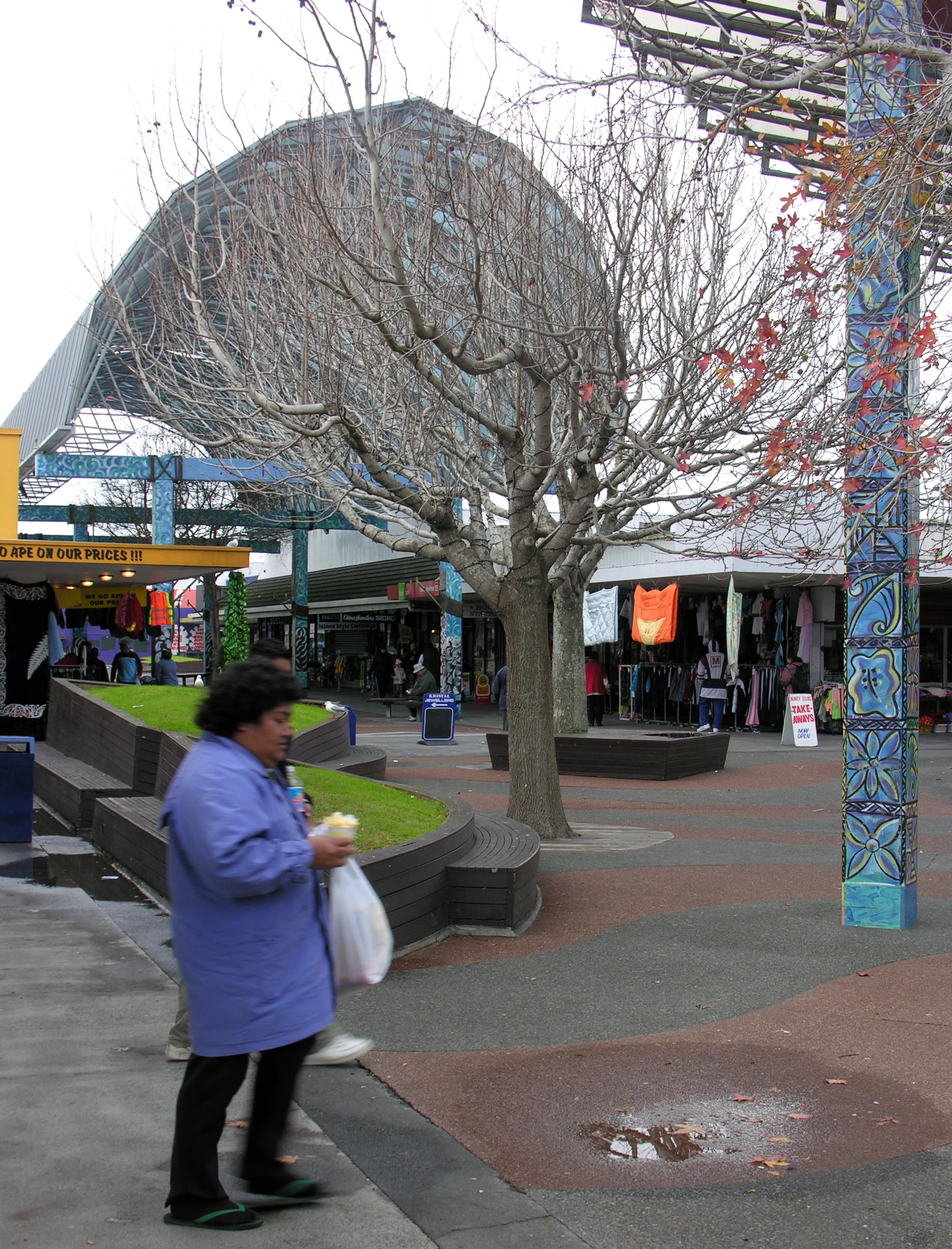 a woman walking past shops near a tall tree