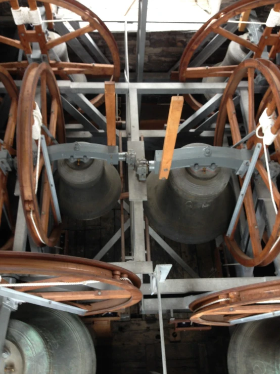 several metal bells and wooden wheels on a machine