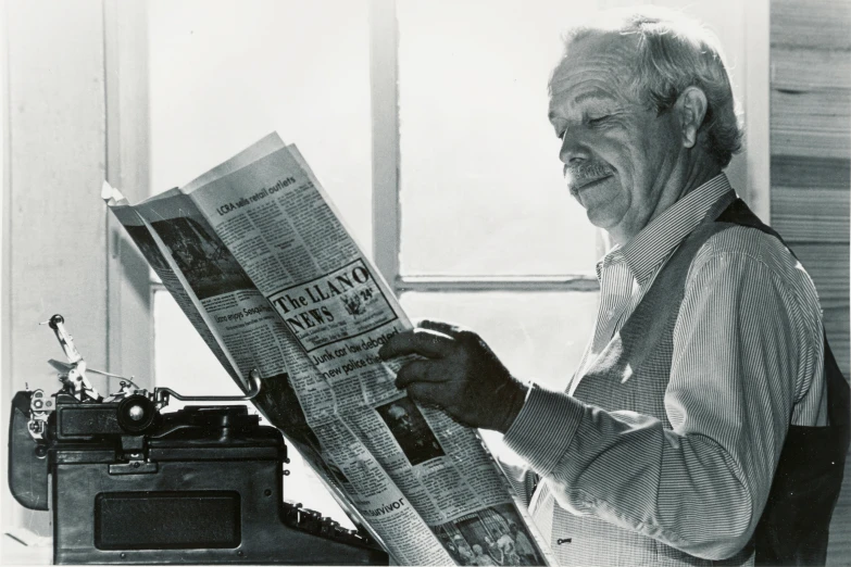 an elderly man holding up the front page of a newspaper