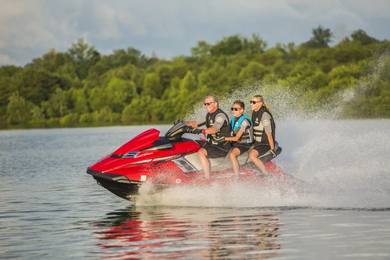 three people are riding on a red jet ski and splashing