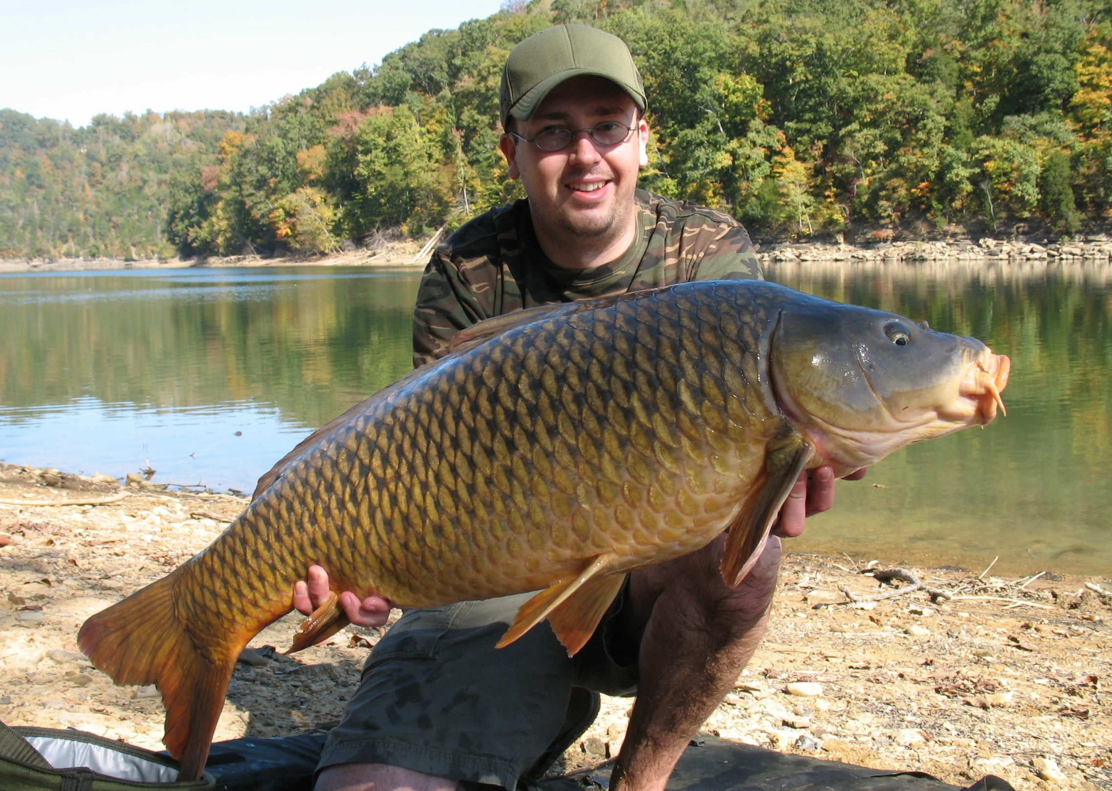 a man kneeling on a river bank while holding a large fish