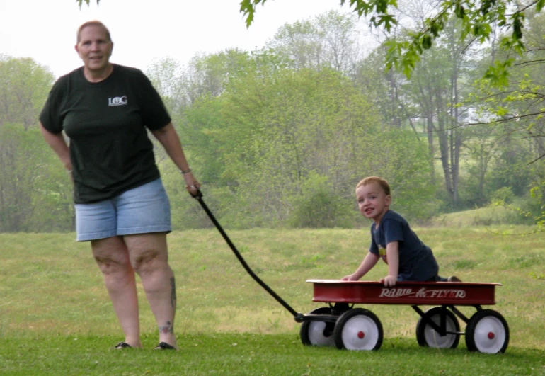 a woman holding a black dog on a leash and pulling a red wagon