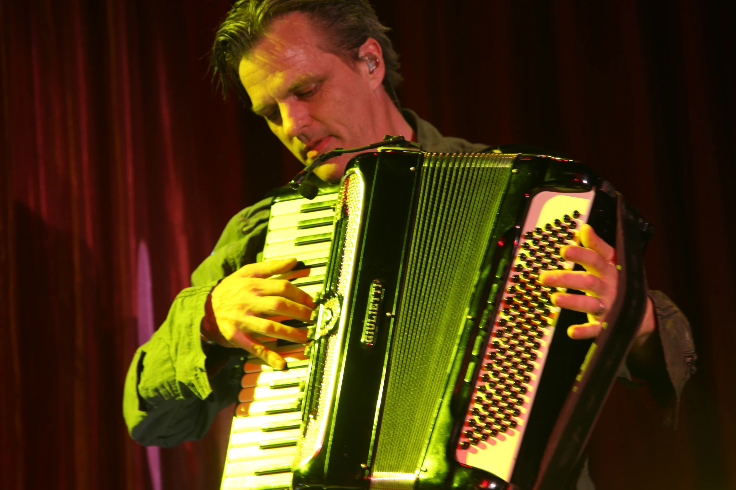 a man that is playing an accordion in front of red curtains