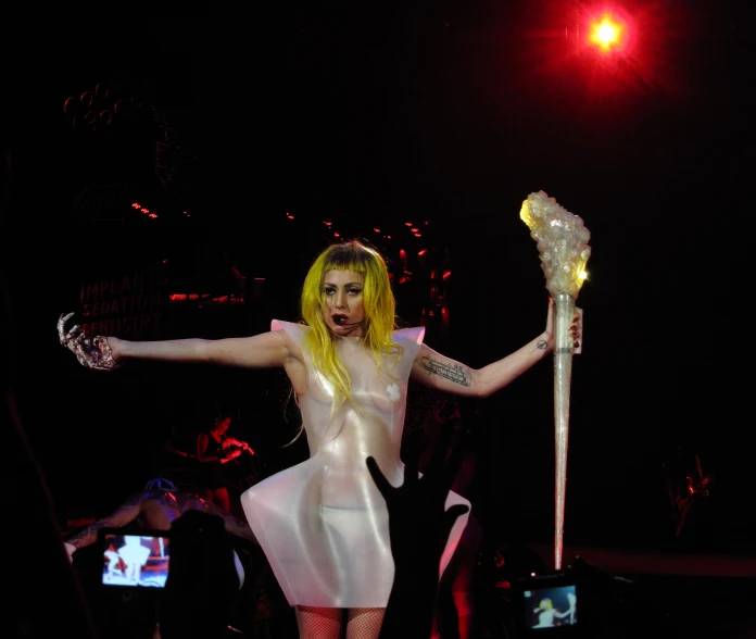 the blond woman wearing her white dress holds up a pole