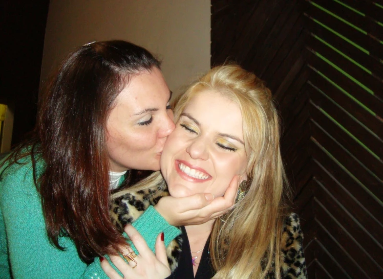 two young women sharing a kiss as one woman stands nearby