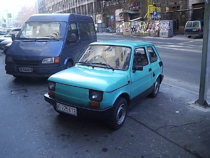 the small car is parked in front of a van