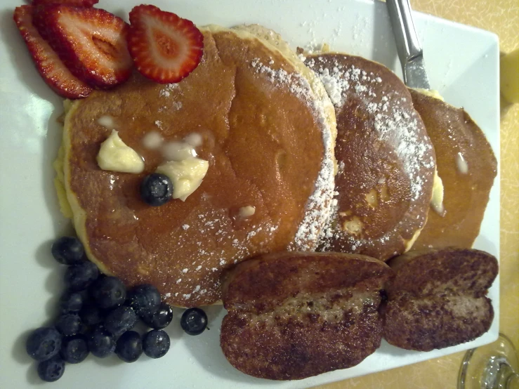 pancakes, berries and ice cream are arranged on a plate