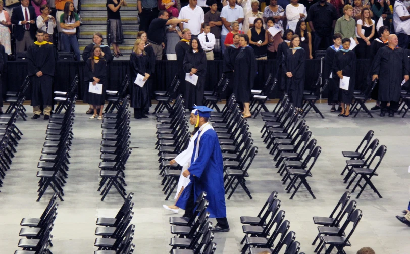 two students dressed in gowns and commencement hats walking toward the front of the stadium