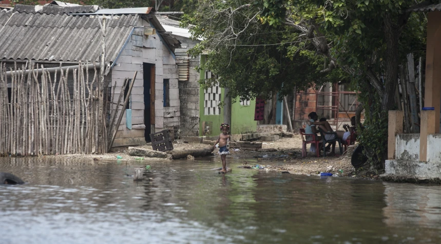 two children wade through water in front of houses