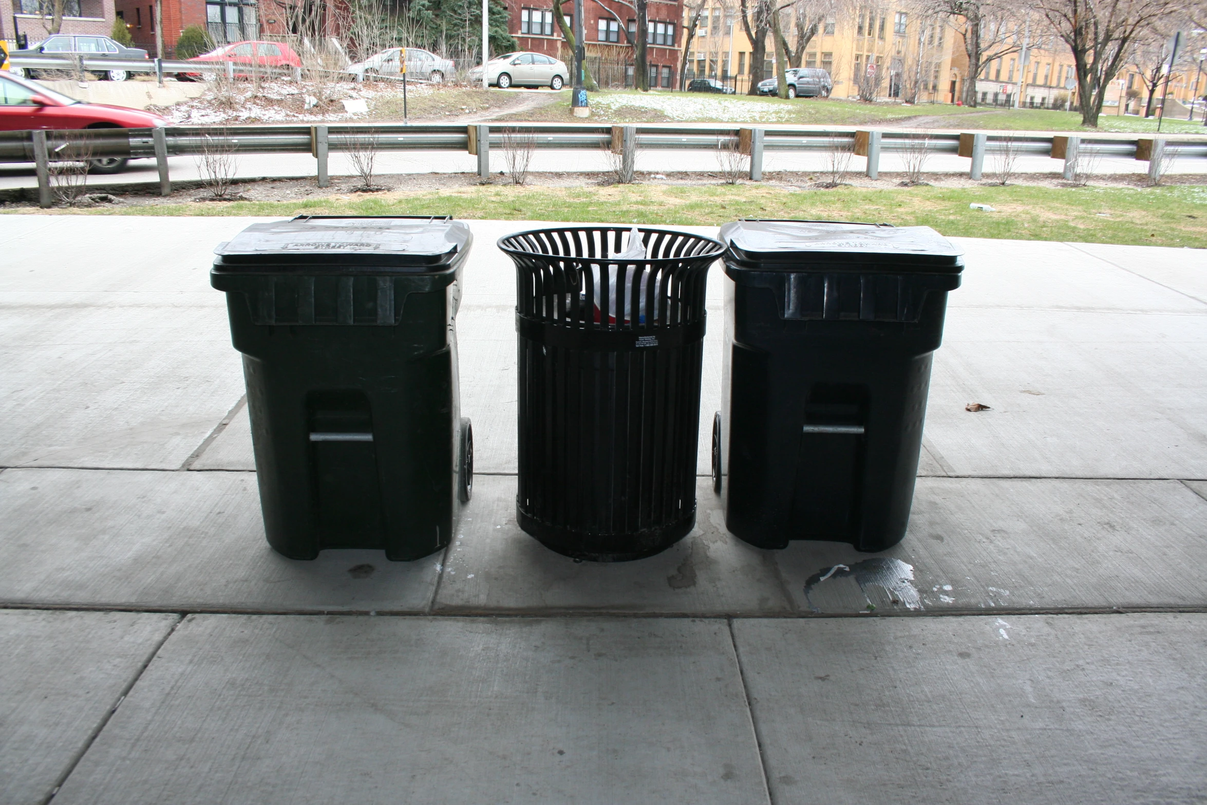 two black trash cans sitting on the sidewalk