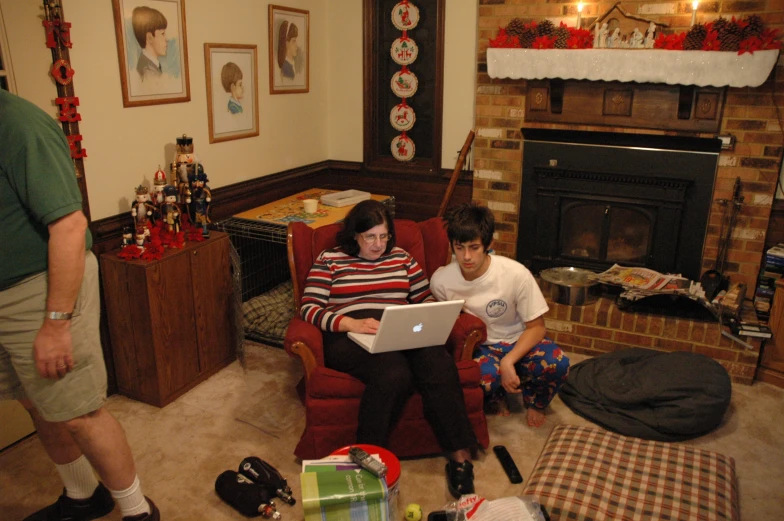 a group of people sit in a living room and look at a laptop