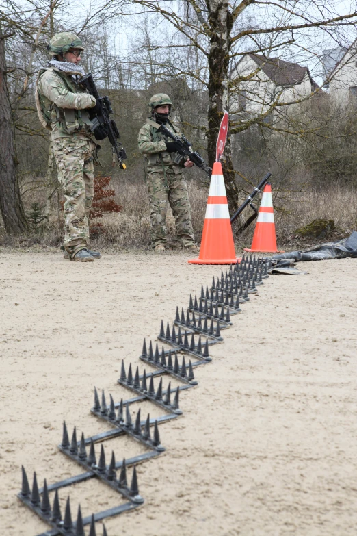 two men with guns in the sand near a row of cones