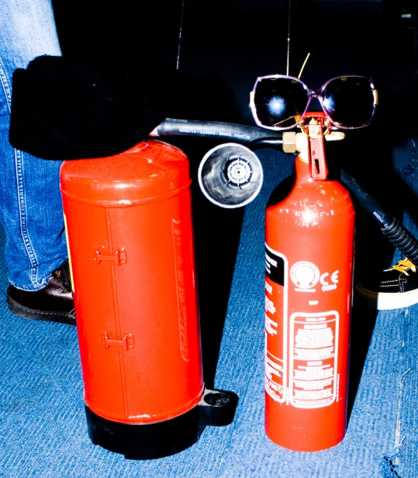 two red cans with sunglasses on them sitting on the floor next to an empty beer bottle