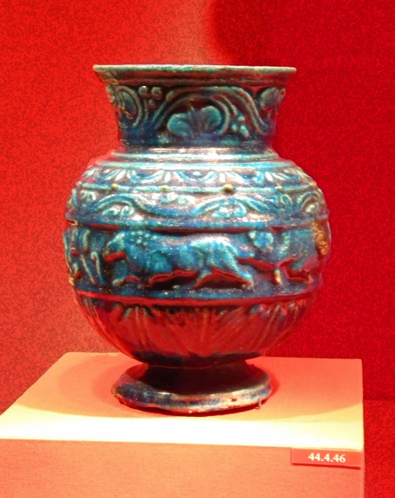 a blue and orange vase on display against red wall