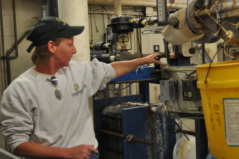 a man in a cap points at machinery that is producing soap