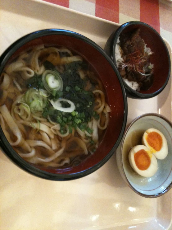 there is a table topped with a white tray and a black bowl filled with noodles