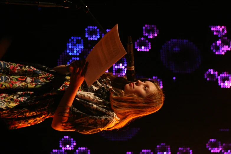 a woman holding a paper standing next to a microphone