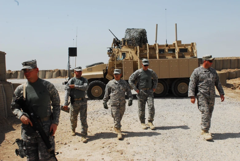 a group of soldiers walking through the desert towards a military vehicle