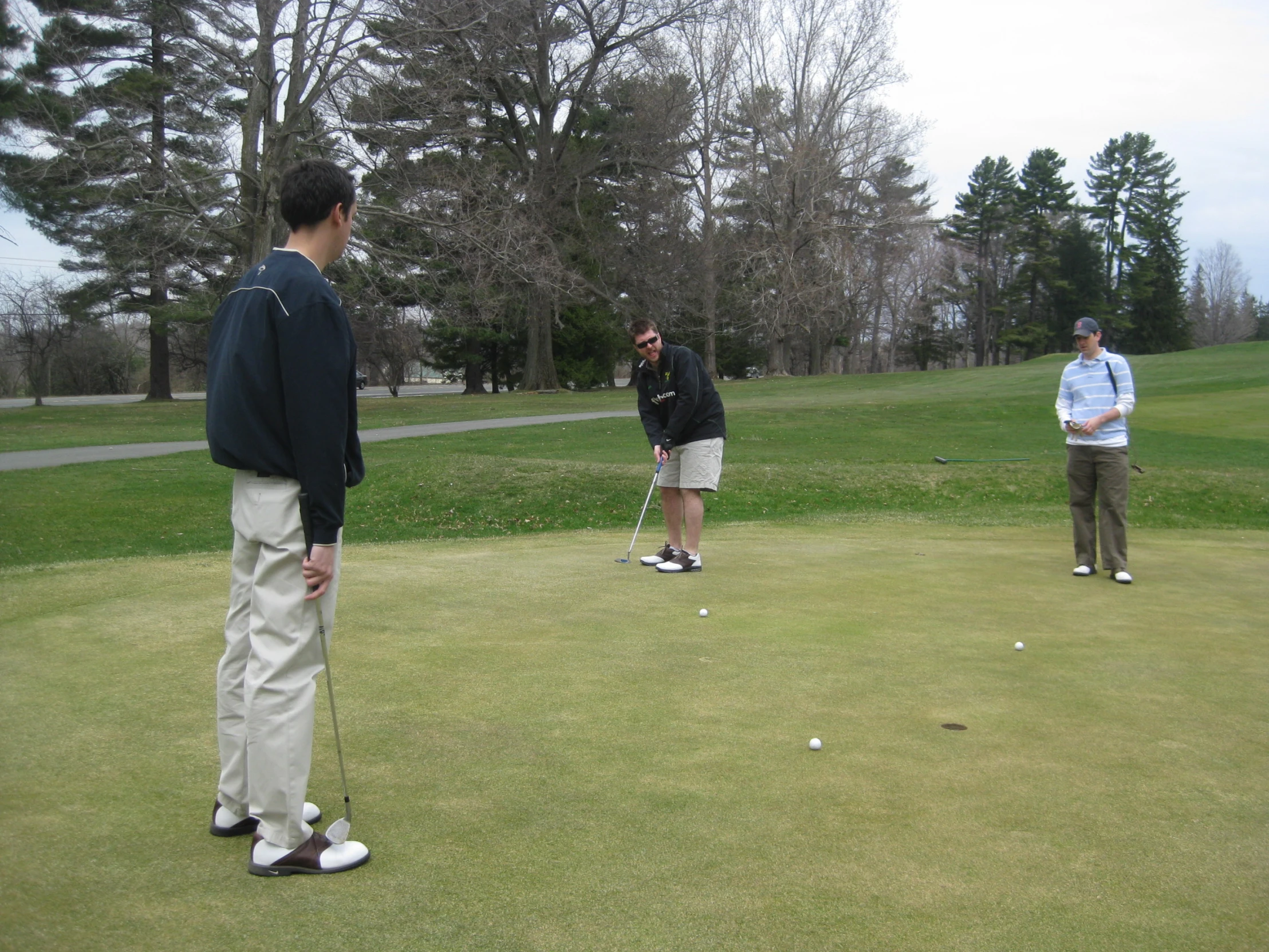 three men playing golf on the green in a park