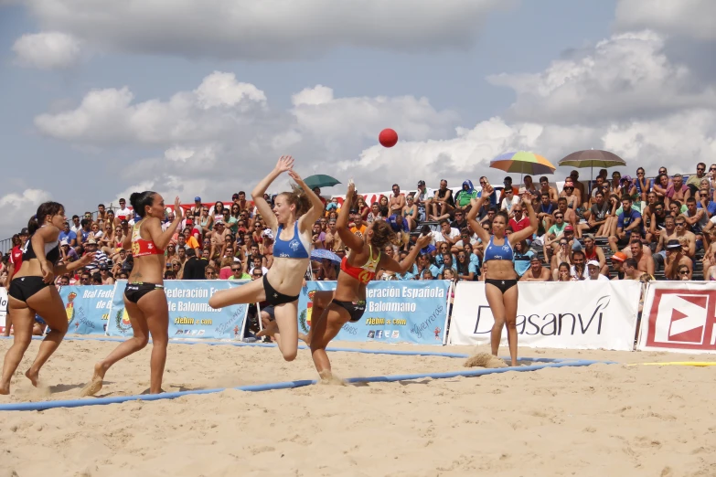 several women in bikinis play with a ball in the sand