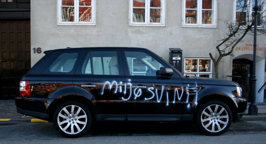 a black land rover with graffiti on the hood parked in front of a building