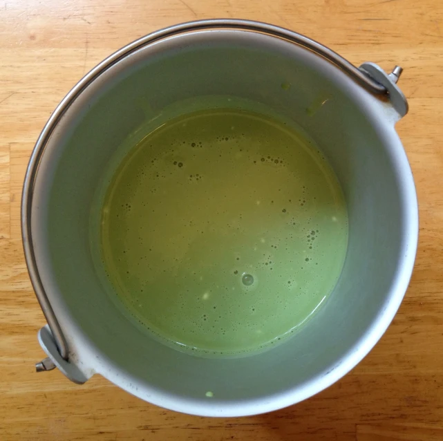 a bowl filled with green liquid on top of a wooden table