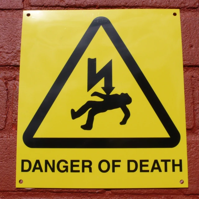 a yellow danger sign hanging on a brick wall