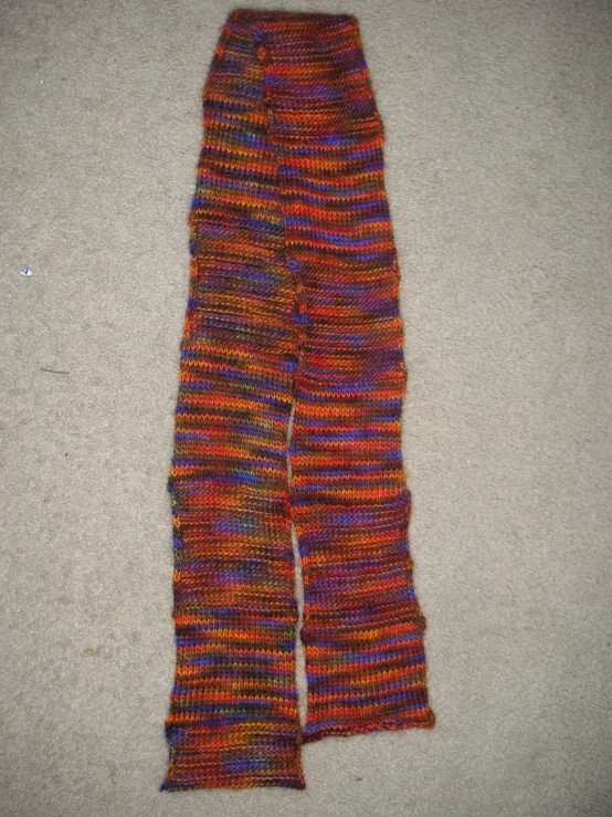 an old multi - colored hand knit scarf sitting on the floor