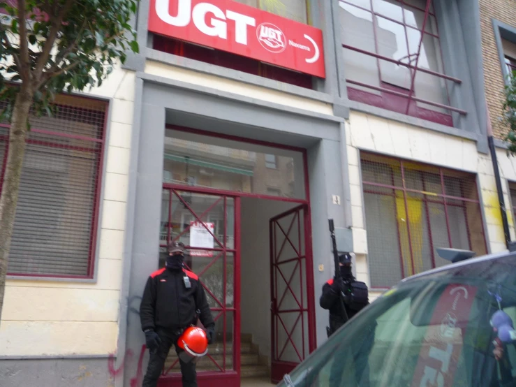 two men with guns stand outside the front door of a building