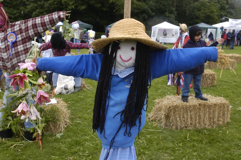 a scarecrow with an enormous hat, blue sweater and a straw hat