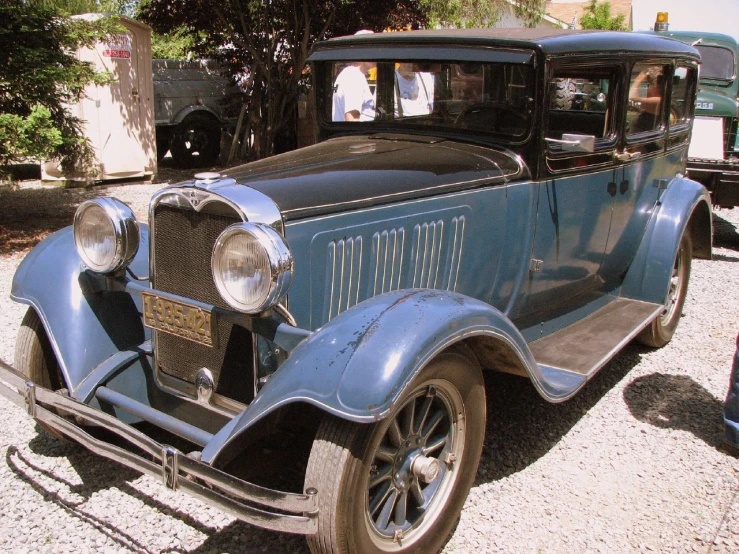 an old blue car parked on top of a gravel lot