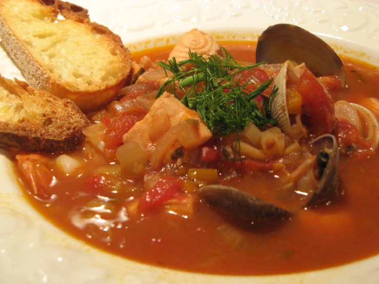 a bowl of soup that has a bread slice and a drink next to it