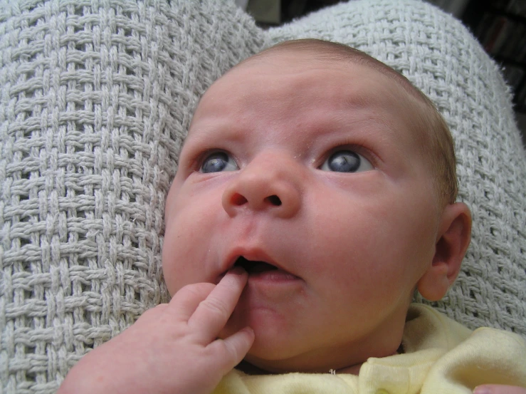 a baby with one eye open and finger in it's mouth