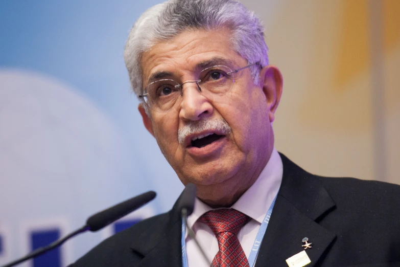 a man wearing glasses speaking into microphone in front of a sign