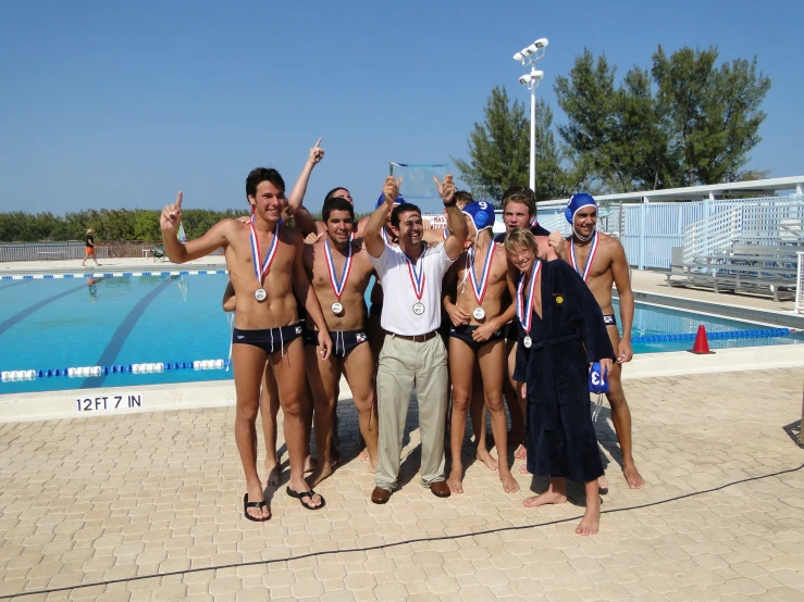 a group of guys and girls standing on the edge of a pool holding medals