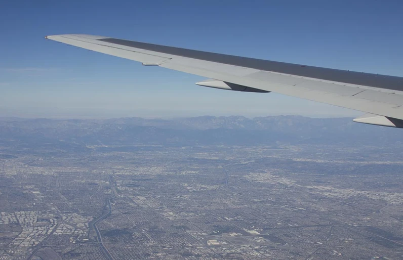 an airplane wing above some buildings and some mountains