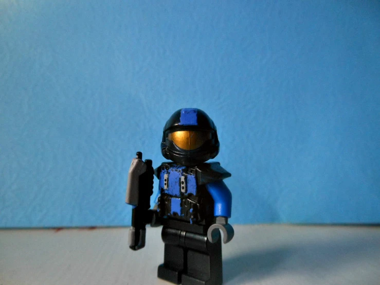 lego figure holding a small gun in front of a blue wall