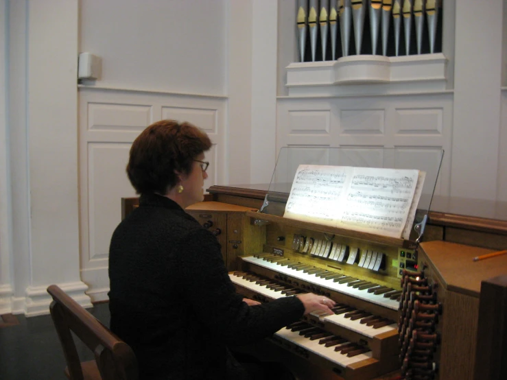 a woman sitting at an organ in front of a pipe organ