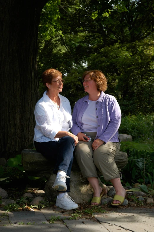 two women sitting on a stone bench near a tree