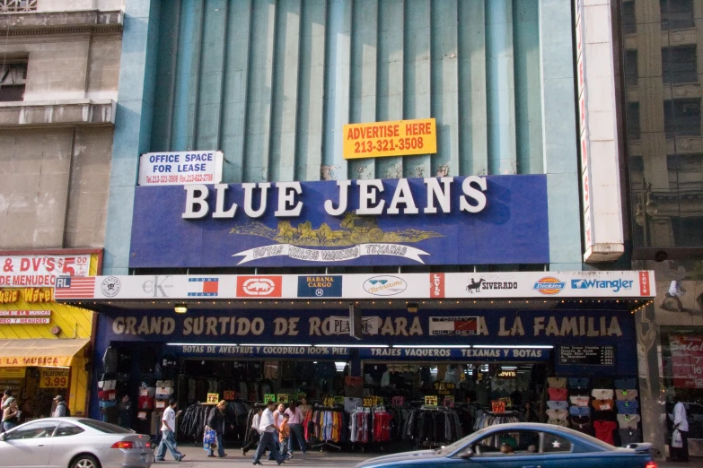 a bunch of people are walking on the sidewalk in front of a blue jeans store